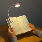 person holding book with clip LED reading light